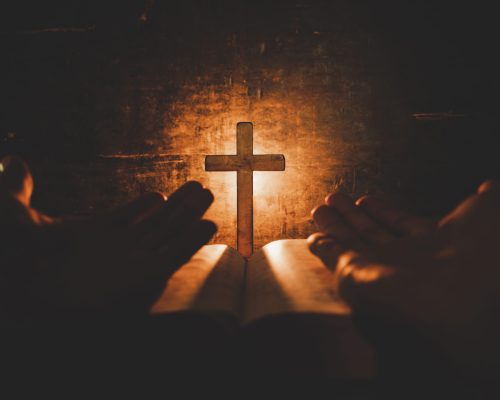 conceptual image focus on candle light with man hand holding wooden cross on bible and blurred world globe in the dark room, christian symbol show Jesus is the light of the world